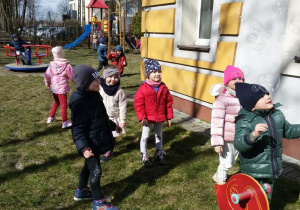 Widok na grupę bawiących się w ogrodzie przedszkolnym dzieci, które obserwują spadające bańki mydlane.